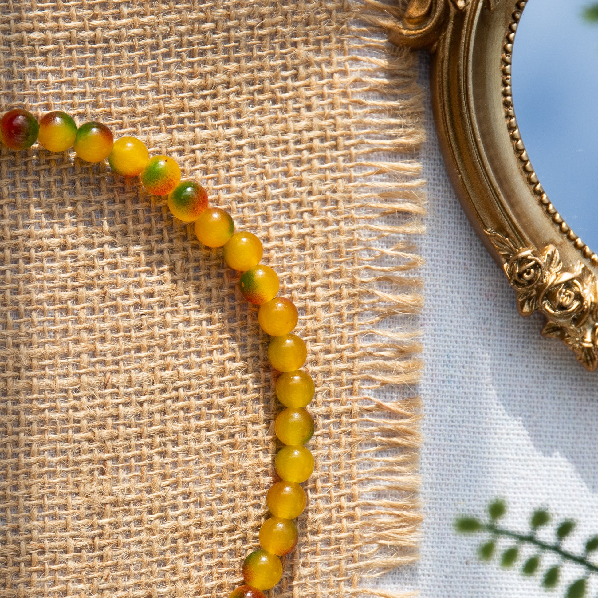 An elastic choker necklace adorned with ombré spray-painted glass beads. The beads' primary colour is golden-yellow, with additional shades of burnt orange and green. Two gold-plated space beads reside in the middle of the choker.
