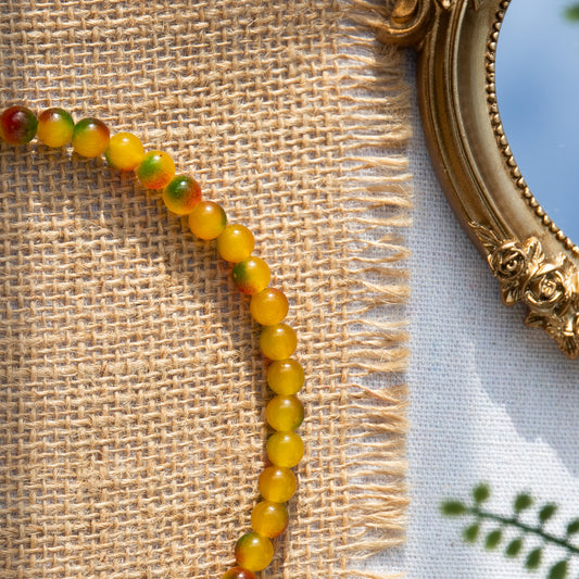 An elastic choker necklace adorned with ombré spray-painted glass beads. The beads' primary colour is golden-yellow, with additional shades of burnt orange and green. Two gold-plated space beads reside in the middle of the choker.