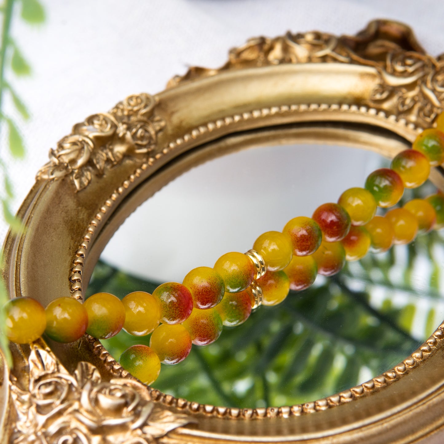 An elastic choker necklace adorned with ombré spray-painted glass beads. The beads' primary colour is golden-yellow, with additional shades of burnt orange and green. Two gold-plated space beads reside in the middle of the choker.