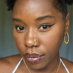 A light gold-toned fake nose ring cuffs the model's nostril. The wire design forms a circular shape. Two seed beads (yellow and lilac) rest below the circle.