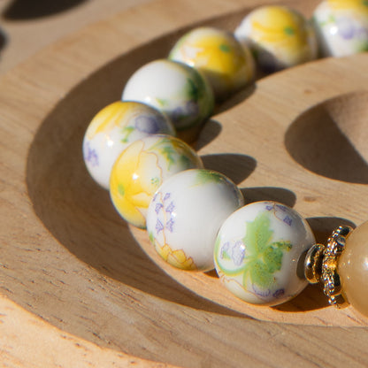 Yellow porcelain beaded bracelet with floral designs on a wooden surface