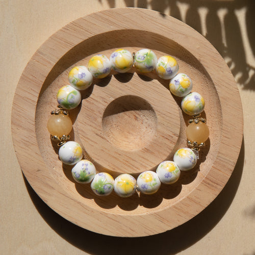Yellow porcelain beaded bracelet embellished with honey jade crystal on a wooden tray with a shell in the background.