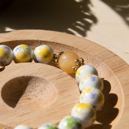 Yellow porcelain beaded bracelet embellished with honey jade crystal on a wooden tray with a shell in the background.