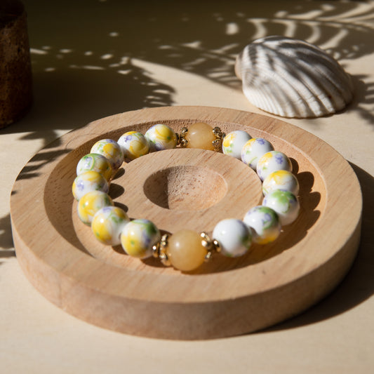 Yellow porcelain beaded bracelet embellished with honey jade crystal on a wooden tray with a shell in the background.