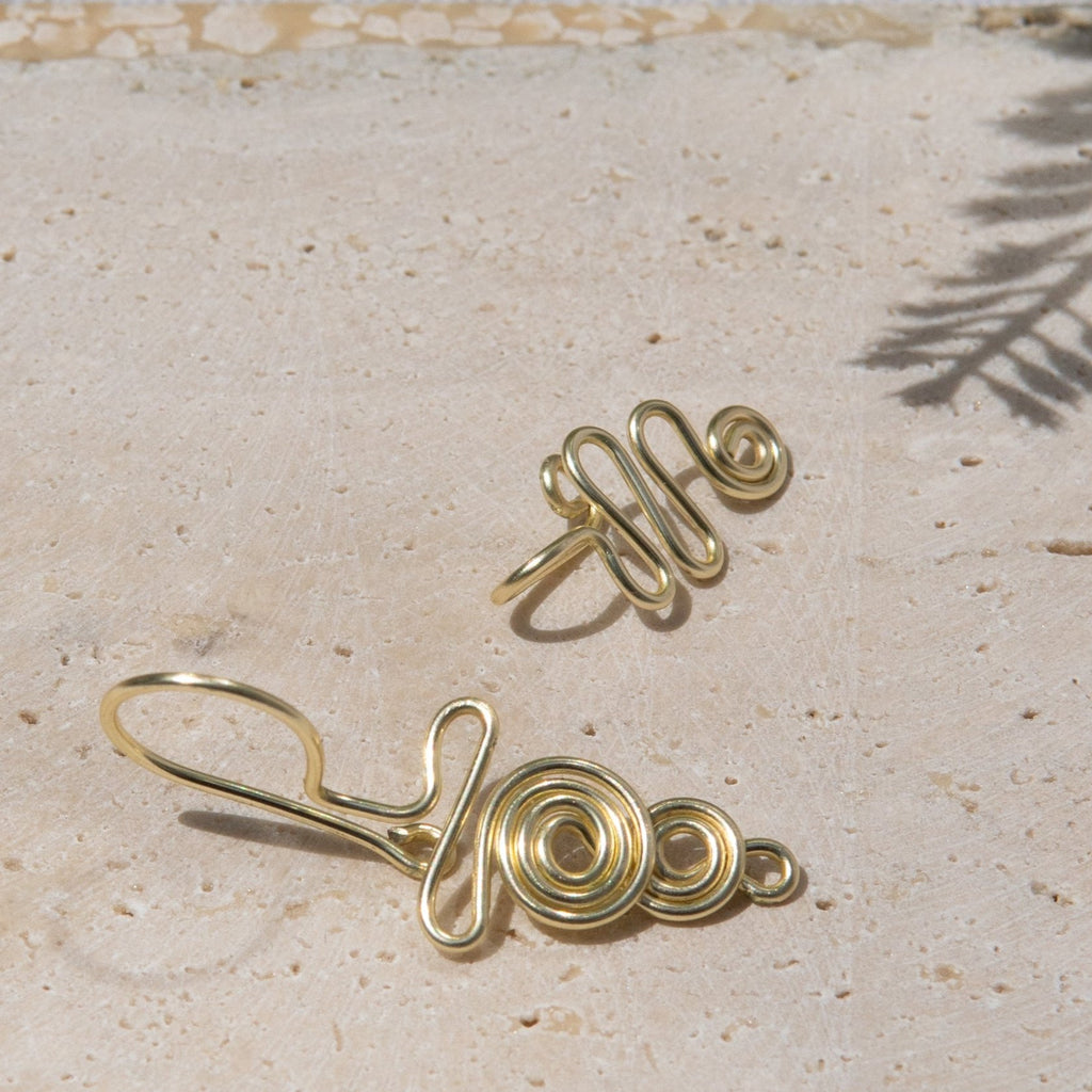 This is a gold-toned faux lip ring made with light gold copper wire. The flexible wire is tightly moulded to form a circular spiral shape that gradually decreases in size. The lip cuff is paired with a light gold faux nose ring. The design starts with a tightly formed circle that gradually swivels in a wavy style.