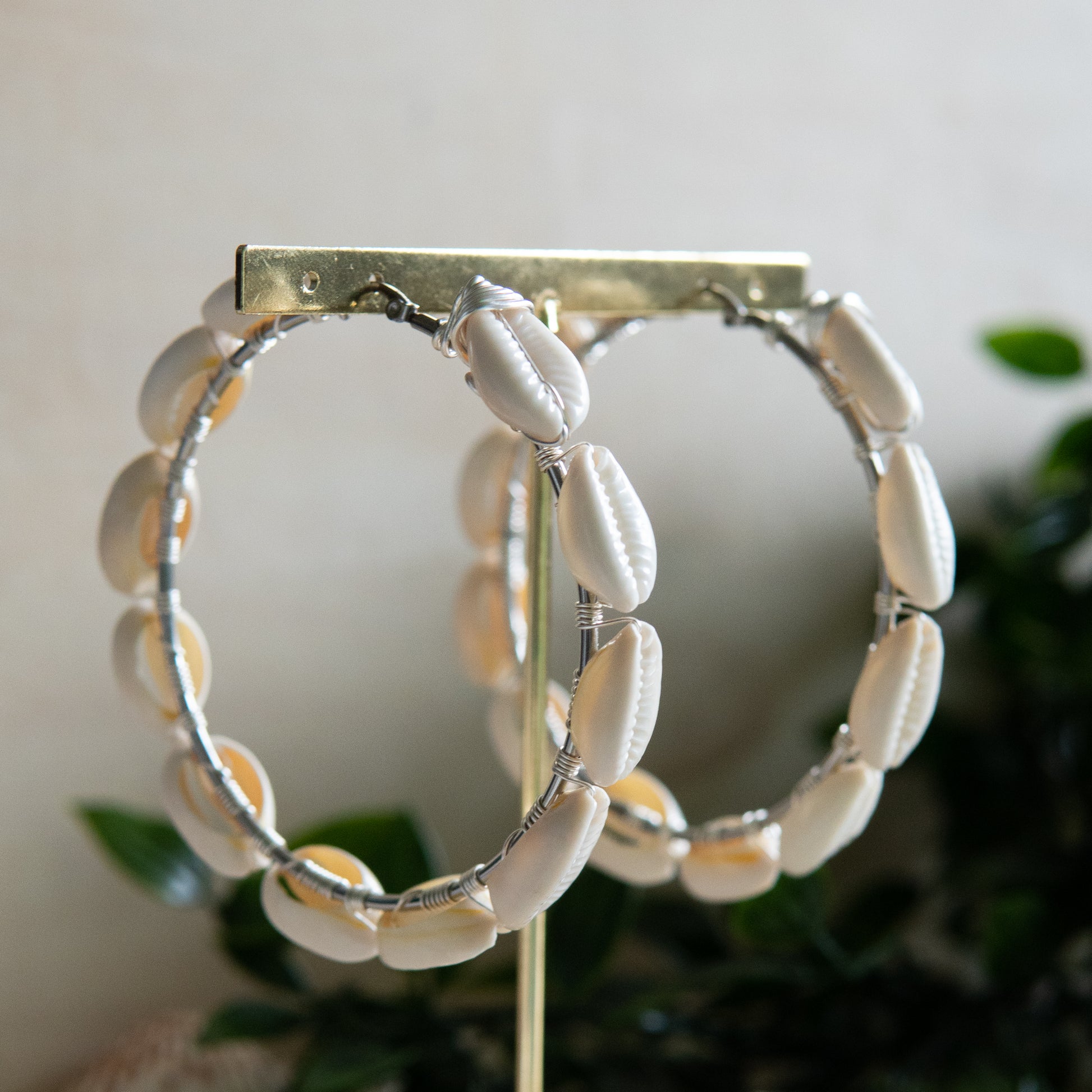 Large silver hoop earrings with cream-toned natural cowrie shells tightly wire-wrapped around the design's circumference.
