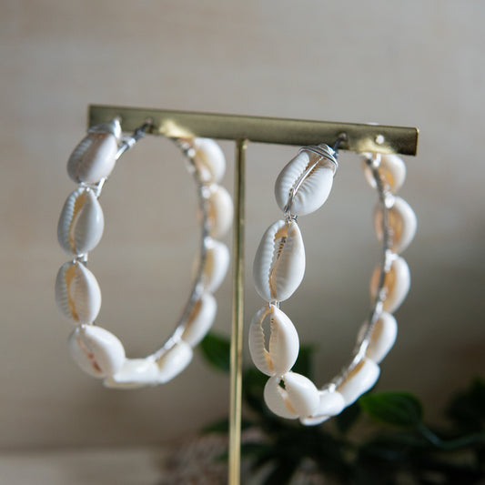 Large silver hoop earrings with cream-toned natural cowrie shells tightly wire-wrapped around the design's circumference.