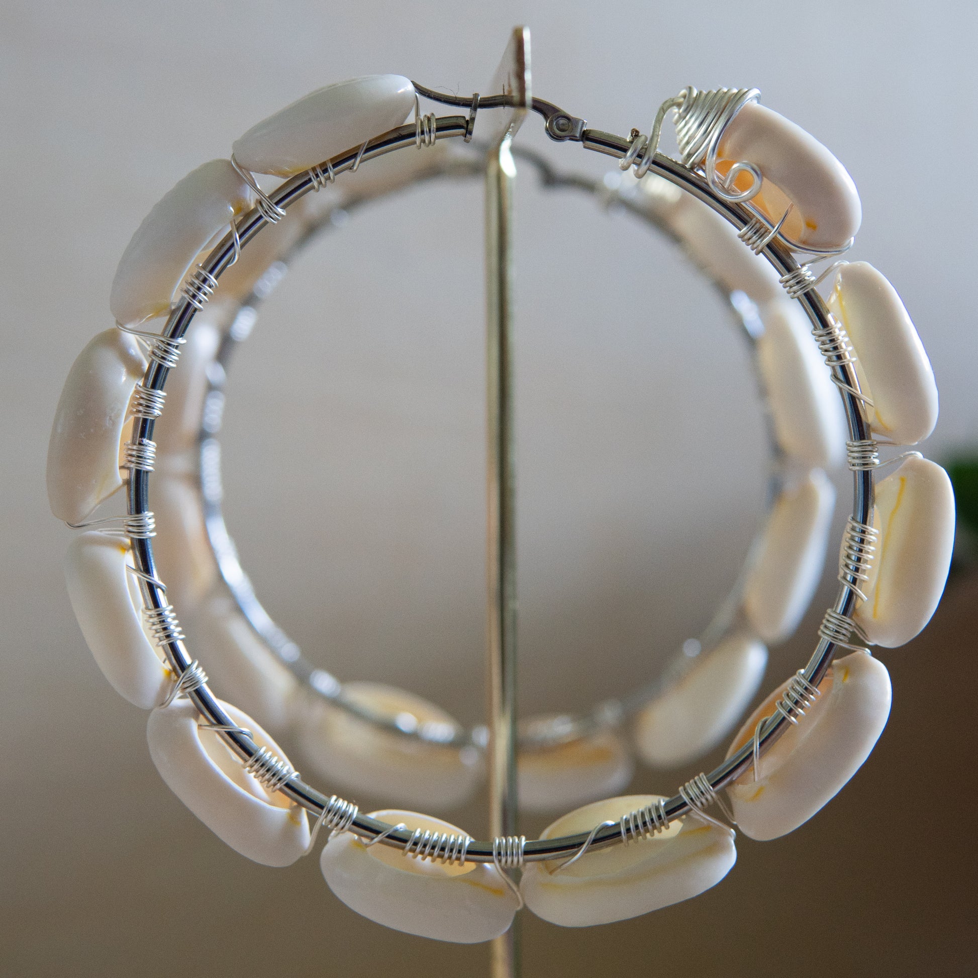 Large silver hoop earrings with cream-toned natural cowrie shells tightly wire-wrapped around the design's circumference.