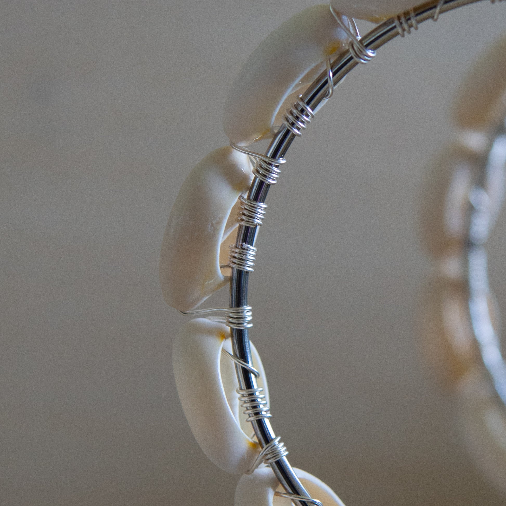 Large silver hoop earrings with cream-toned natural cowrie shells tightly wire-wrapped around the design's circumference.