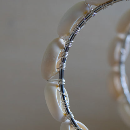 Large silver hoop earrings with cream-toned natural cowrie shells tightly wire-wrapped around the design's circumference.