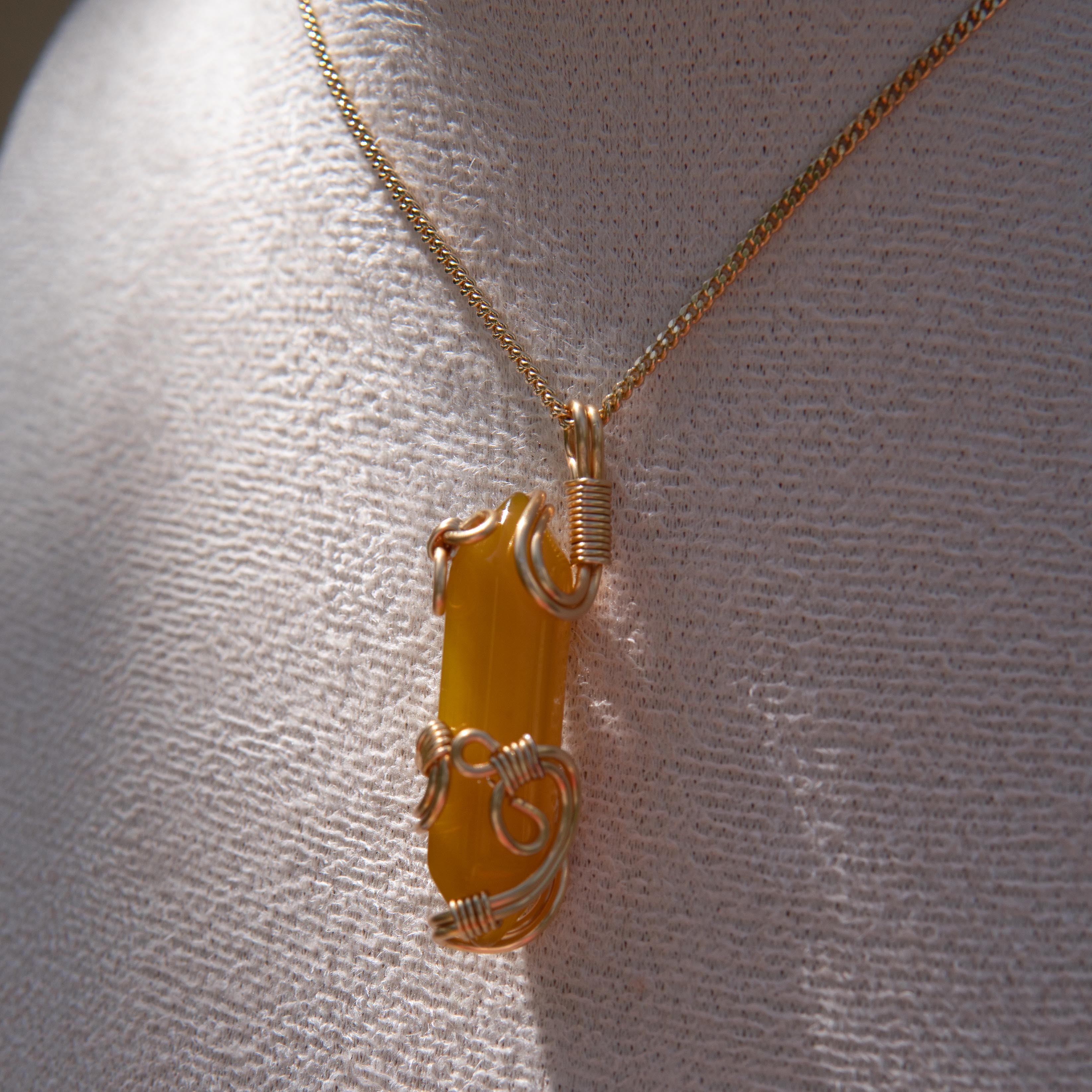 Gold wire-wrapped yellow agate pendant necklace displayed on a white fabric bust