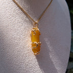 Gold wire-wrapped yellow agate pendant necklace displayed on a white fabric bust.
