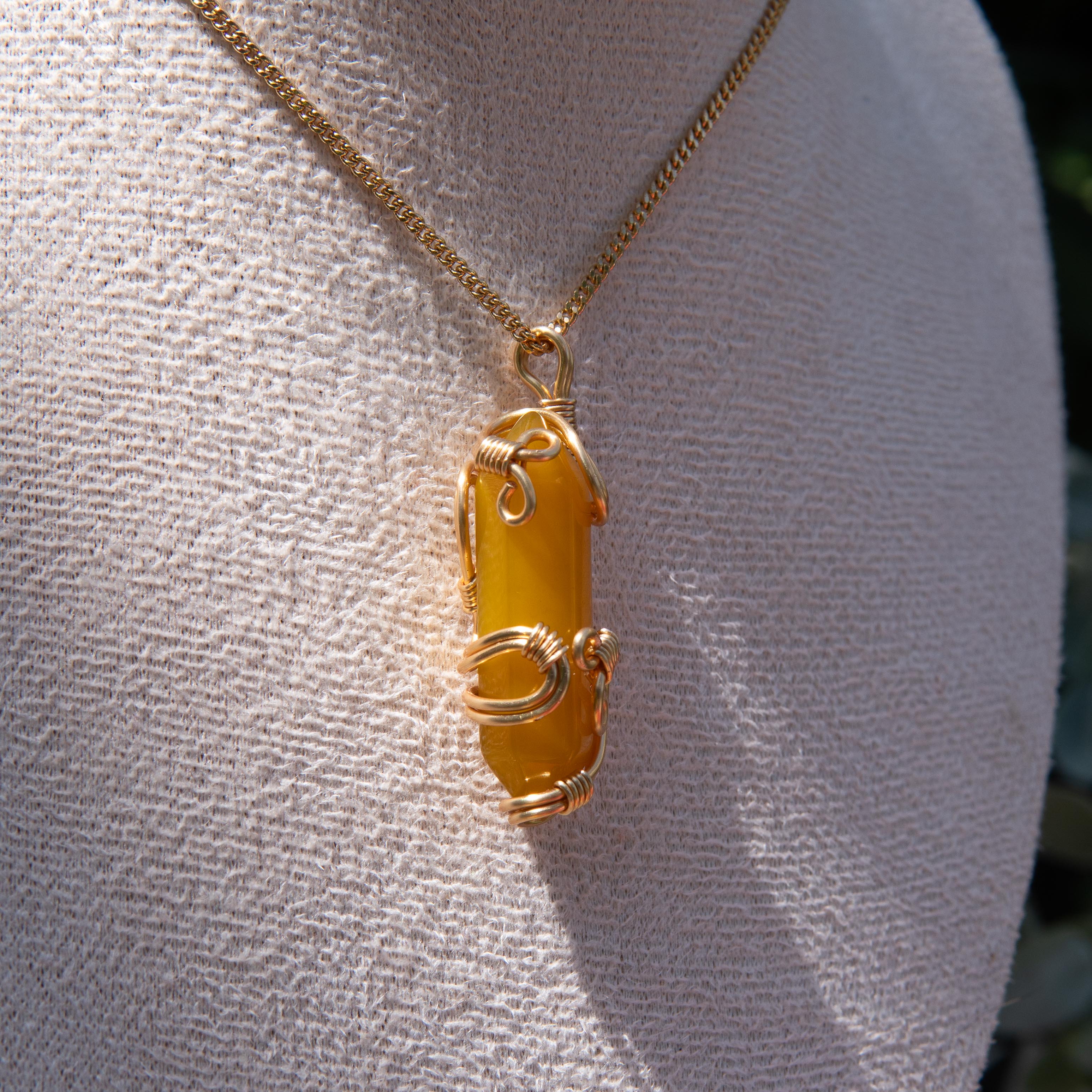 Gold wire-wrapped yellow agate pendant necklace displayed on a white fabric bust.