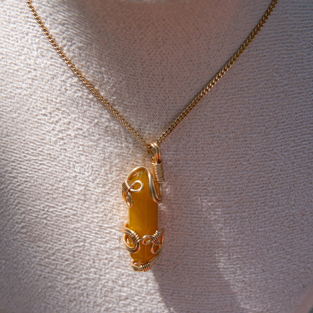 Gold wire-wrapped yellow agate pendant necklace displayed on a white fabric bust