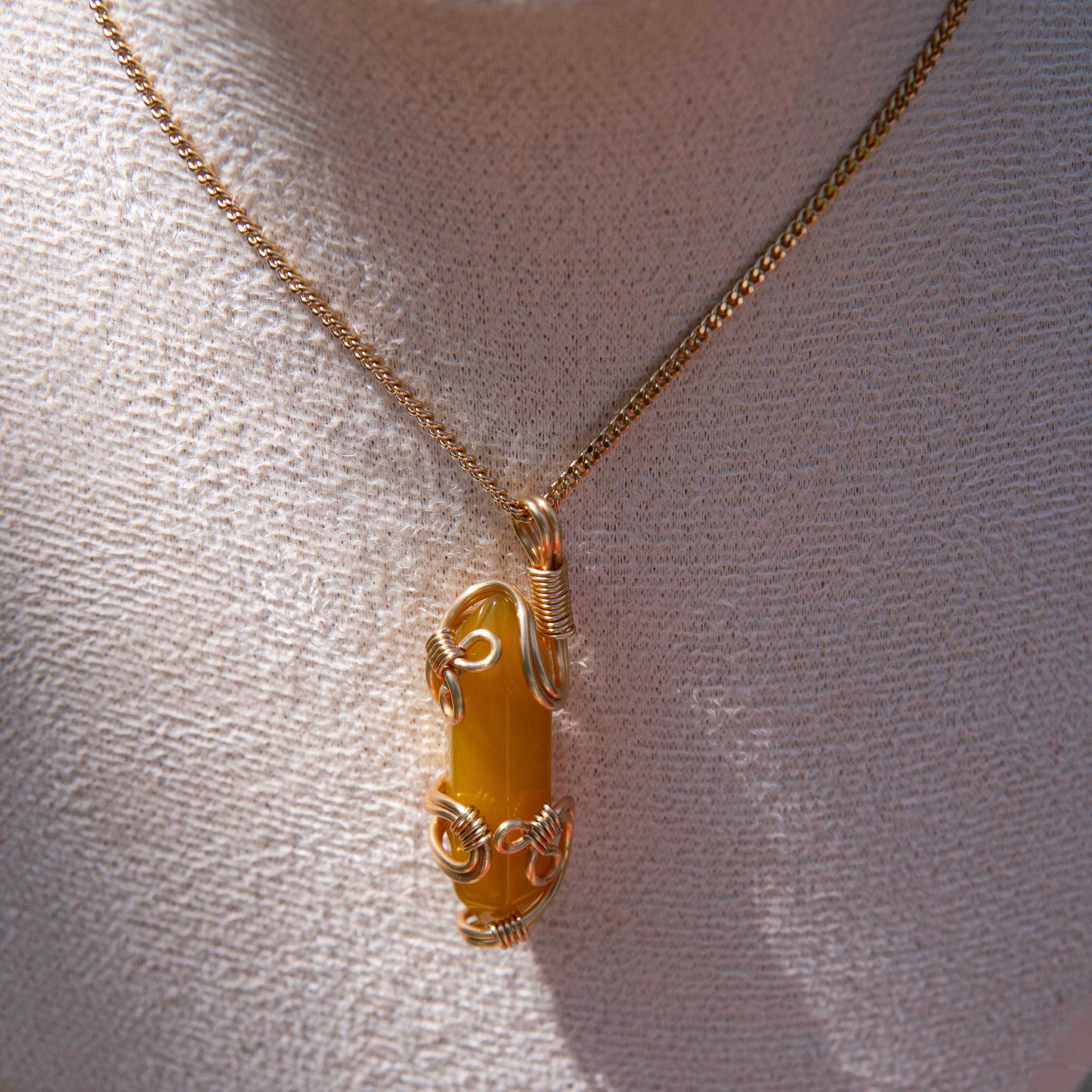 Gold wire-wrapped yellow agate pendant necklace displayed on a white fabric bust