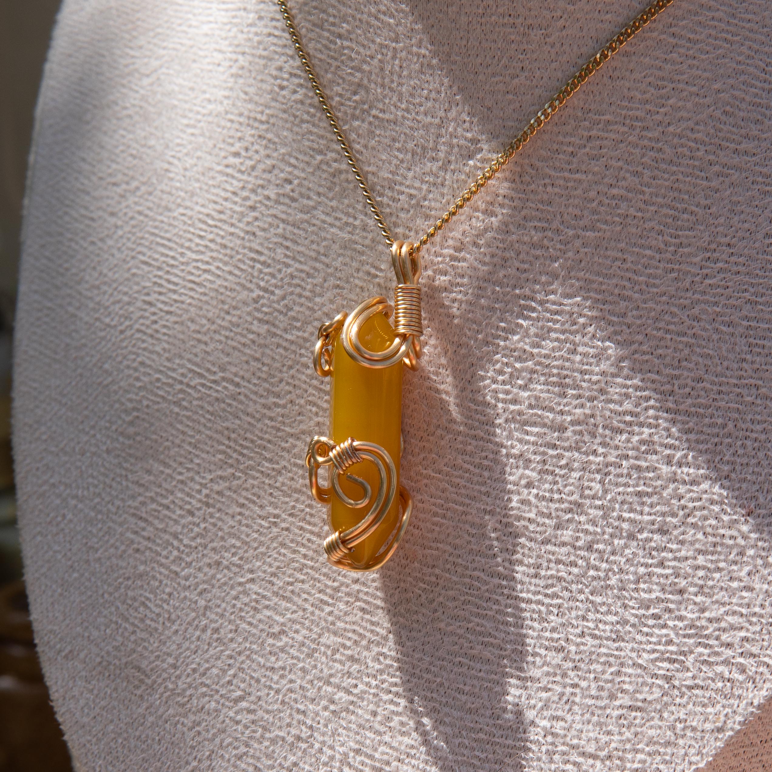 Gold wire-wrapped yellow agate pendant necklace displayed on a white fabric bust