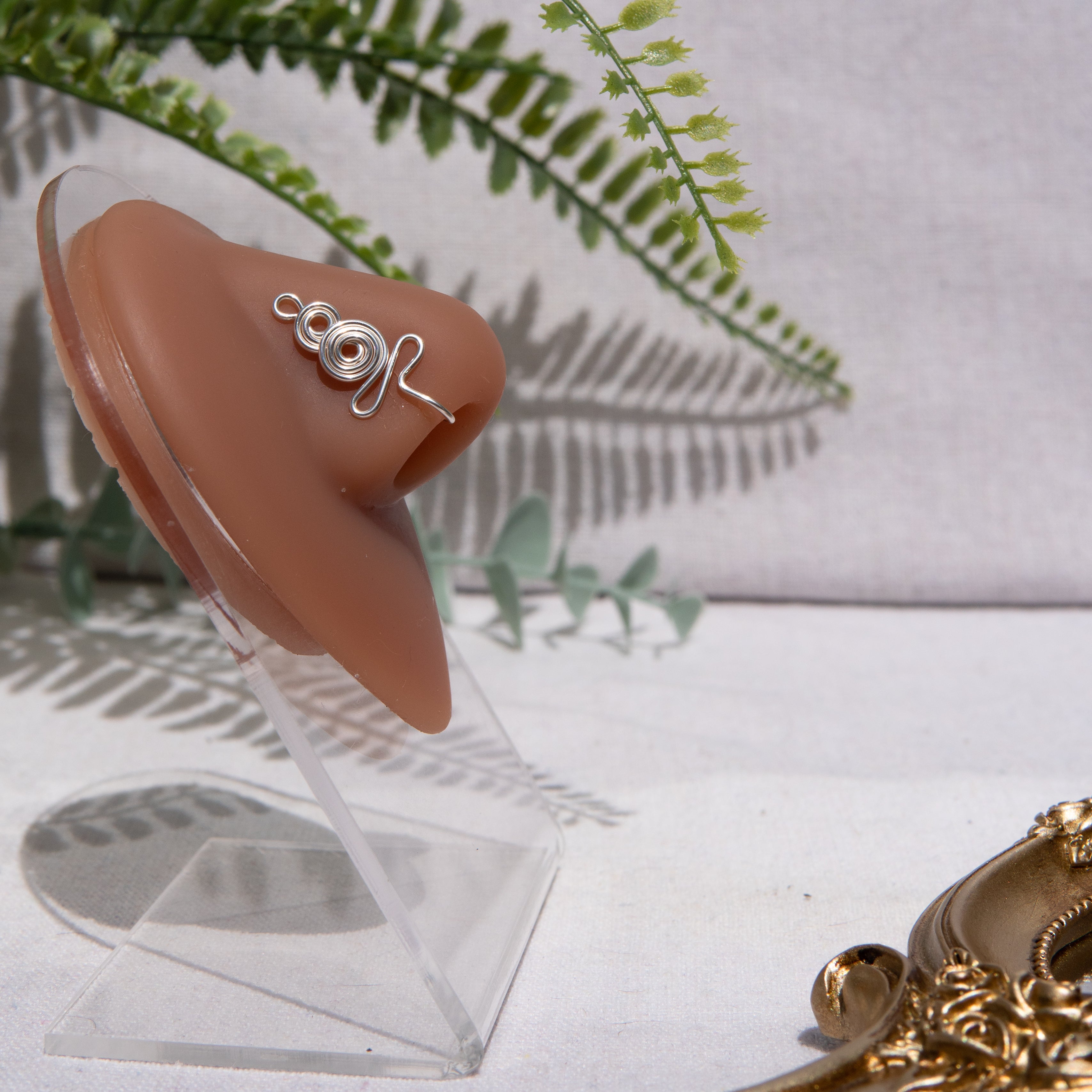 A silver-toned nose cuff adorns the model's nose in a circular wire design that spirals up and gradually decreases in size.