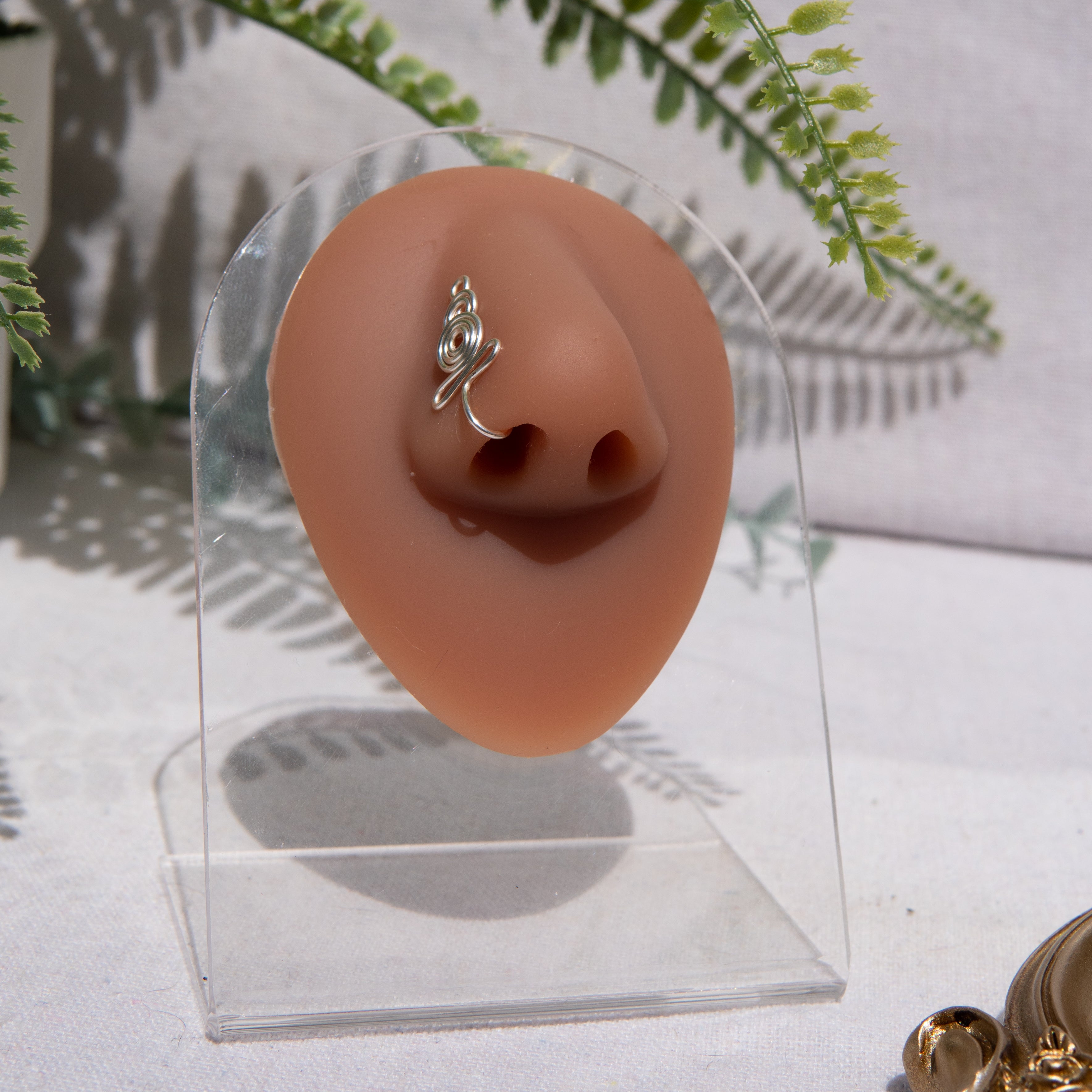 A silver-toned nose cuff adorns the model's nose in a circular wire design that spirals up and gradually decreases in size.