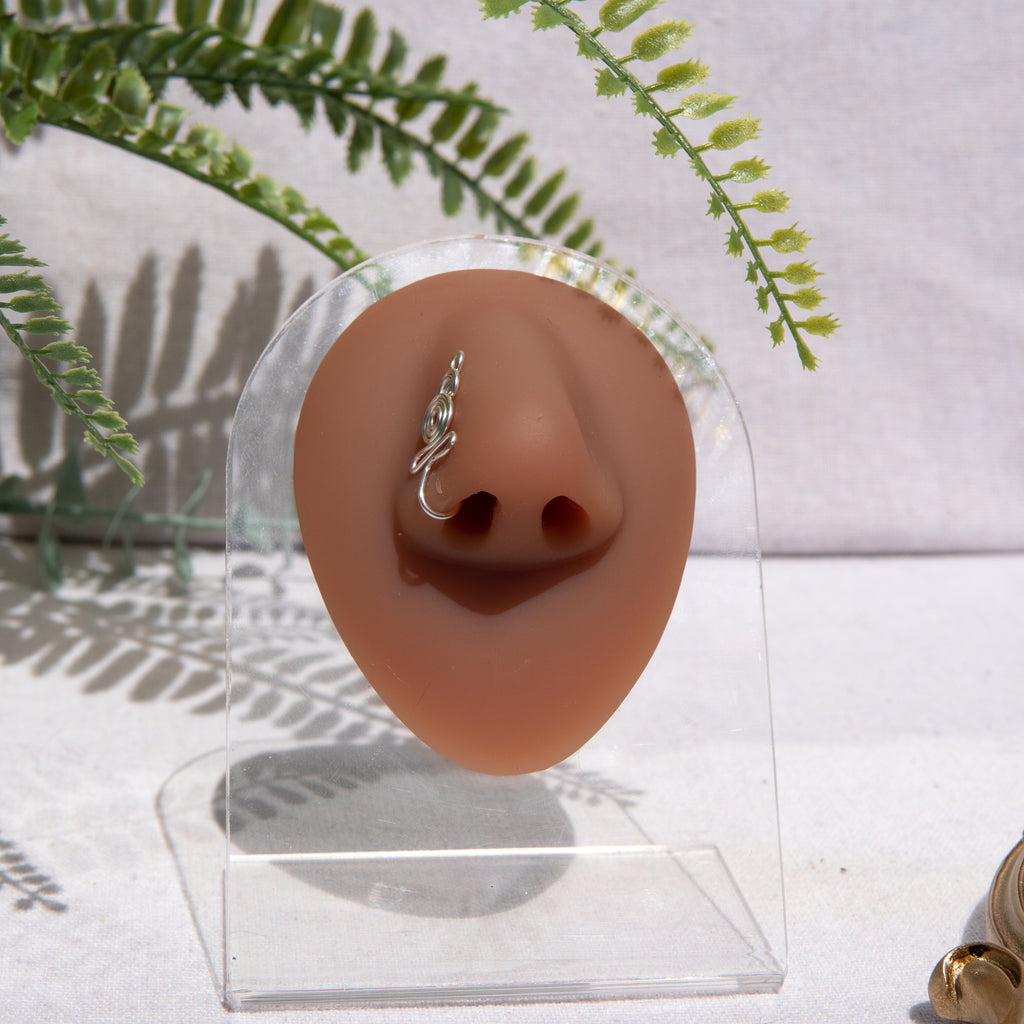 A silver-toned nose cuff adorns the model's nose in a circular wire design that spirals up and gradually decreases in size.