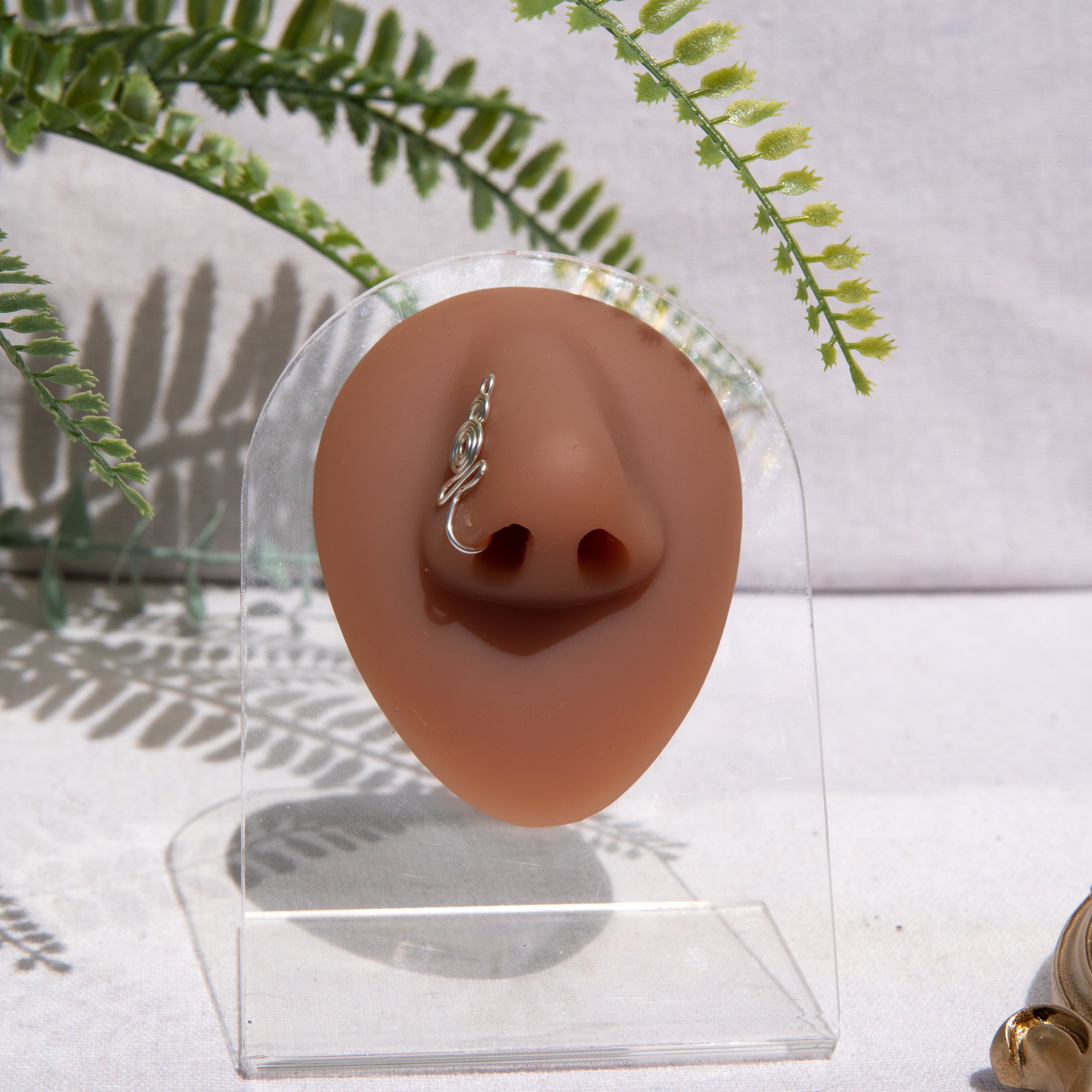 A silver-toned nose cuff adorns the model's nose in a circular wire design that spirals up and gradually decreases in size.