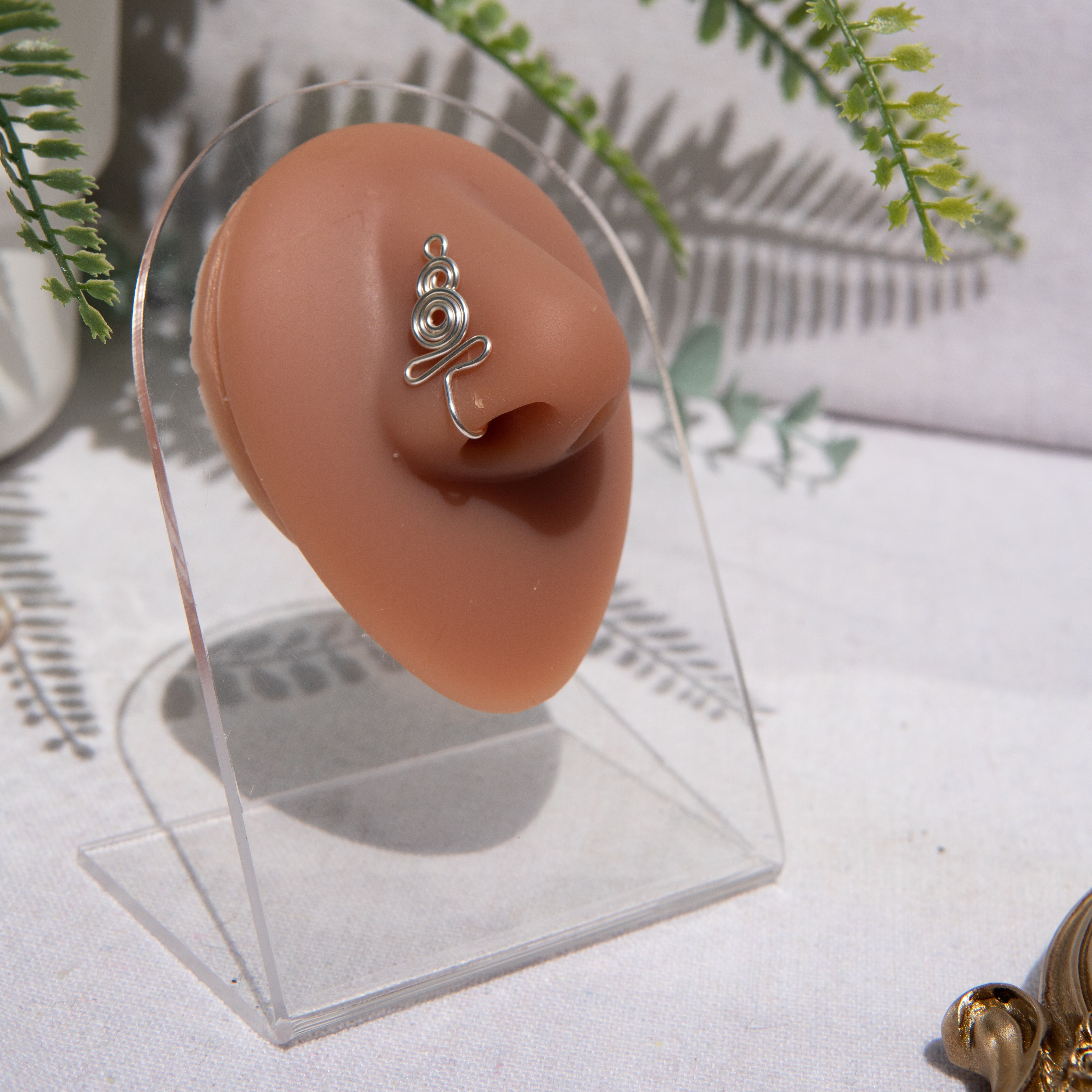 A silver-toned nose cuff adorns the model's nose in a circular wire design that spirals up and gradually decreases in size.