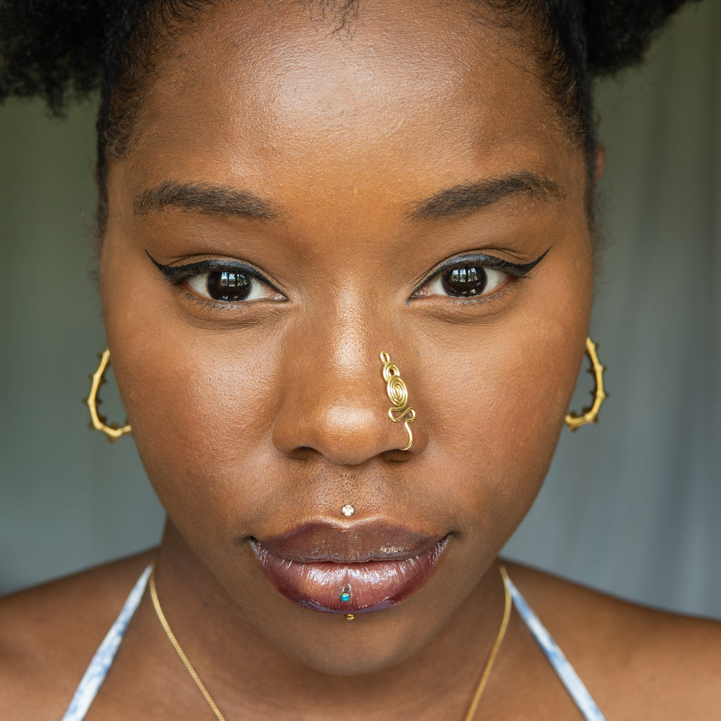 A light gold-toned nose cuff adorns the model's nose in a circular wire design that spirals up and gradually decreases in size.