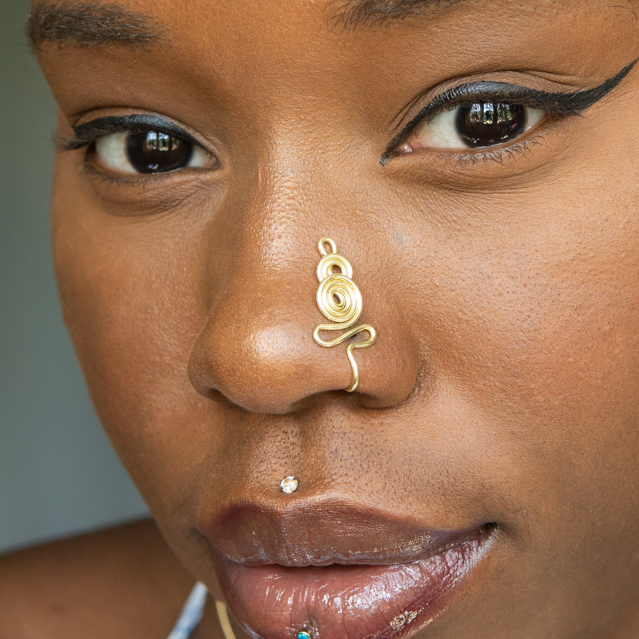 A light gold-toned nose cuff adorns the model's nose in a circular wire design that spirals up and gradually decreases in size.