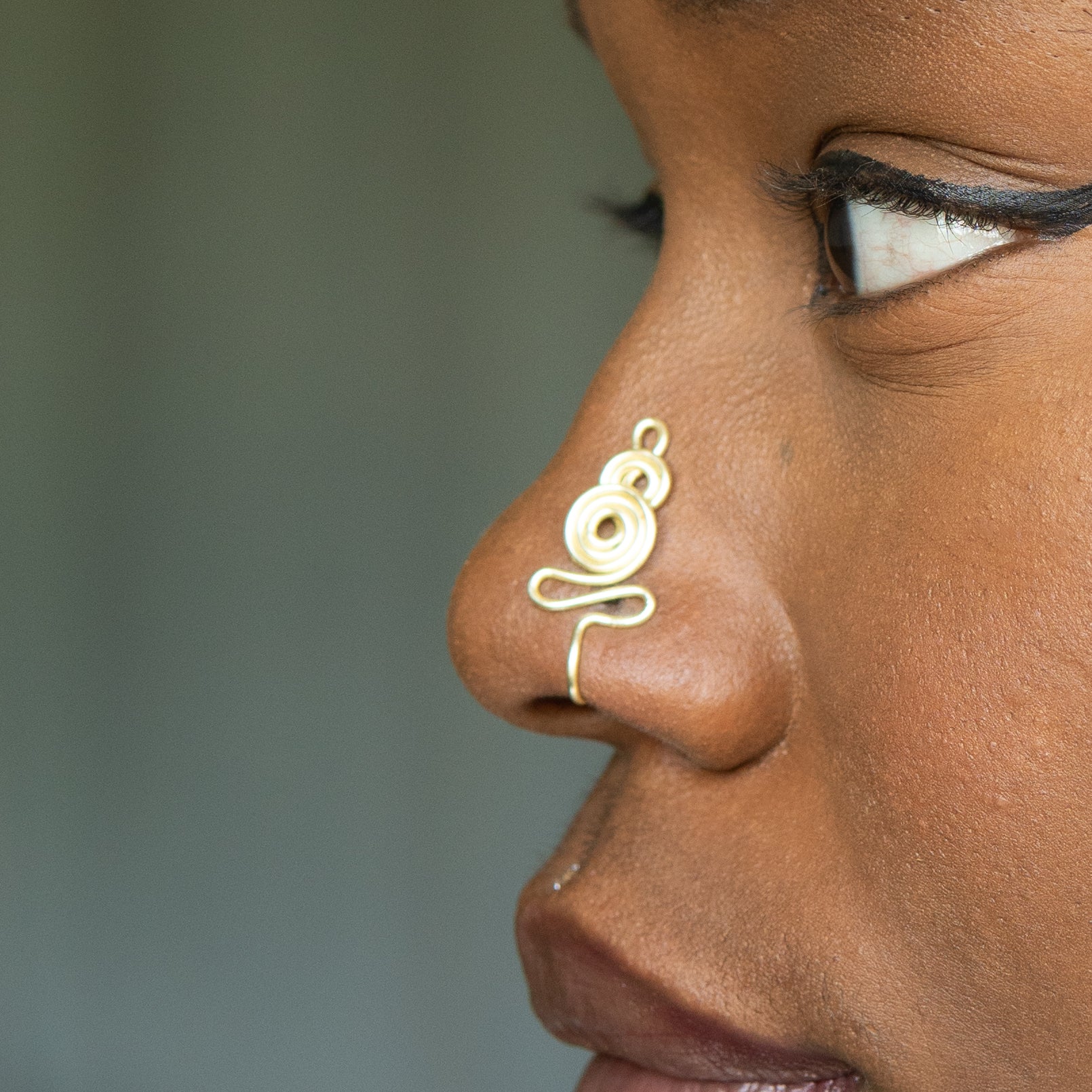 A light gold-toned nose cuff adorns the model's nose in a circular wire design that spirals up and gradually decreases in size.