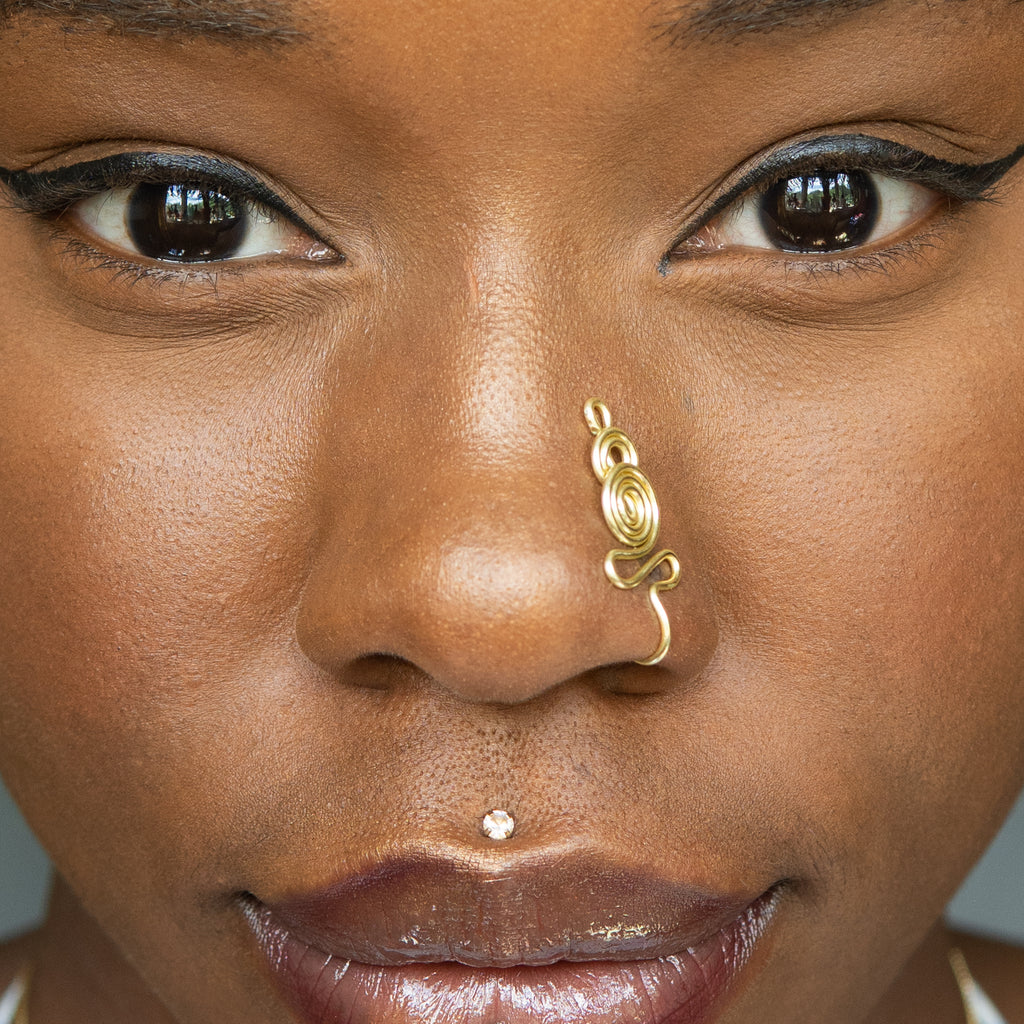 A light gold-toned nose cuff adorns the model's nose in a circular wire design that spirals up and gradually decreases in size.