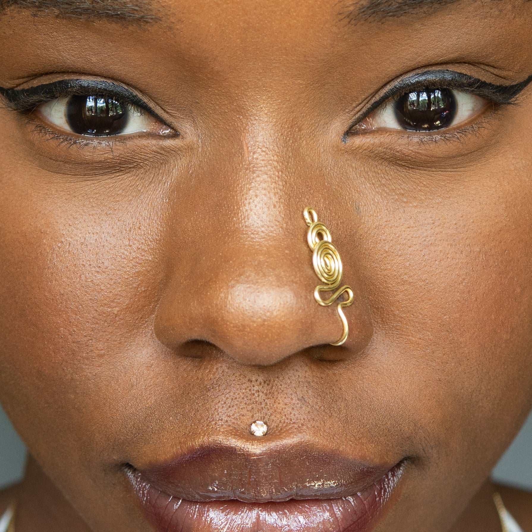 A light gold-toned nose cuff adorns the model's nose in a circular wire design that spirals up and gradually decreases in size.