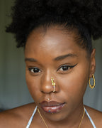 A light gold-toned, tightly spiralled nose cuff rests on the model's nose. Two seed beads (green and lilac) are interwoven into the design as the 3-tier circular spiral gradually decreases in size.