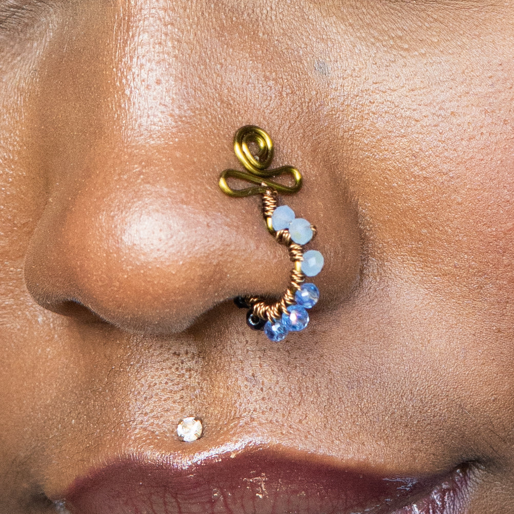 A bronze-toned faux nose ring cuffs the model's nose. Blue transparent seed beads are wire-wrapped around the hoop's circumference. Above the hoop, the wire design forms an Ankh symbol