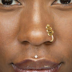 A gold-toned faux nose ring cuffs the model's nose. The wire design moulds a wavy pyramid shape.