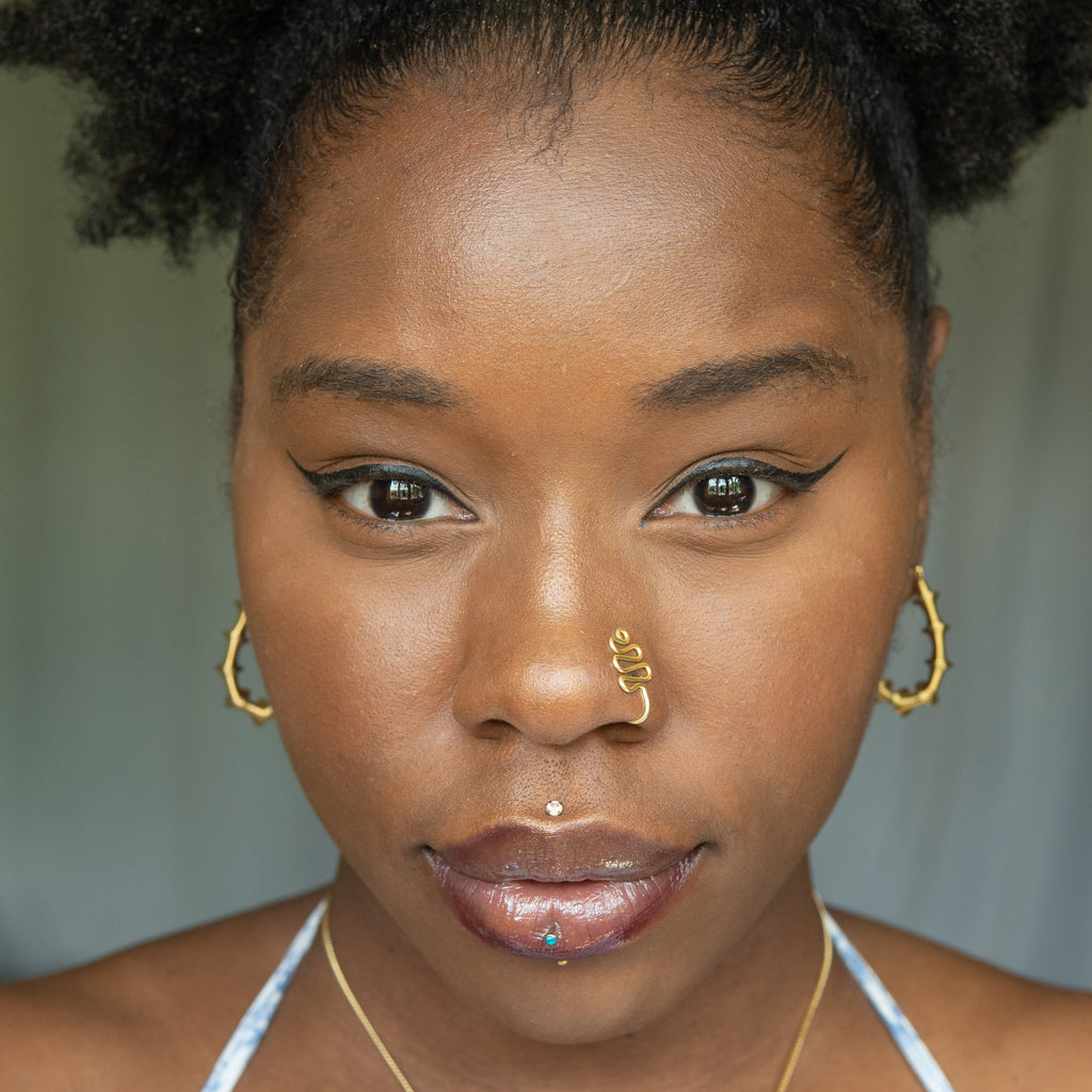 A gold-toned faux nose ring cuffs the model's nose. The wire design moulds a wavy pyramid shape.