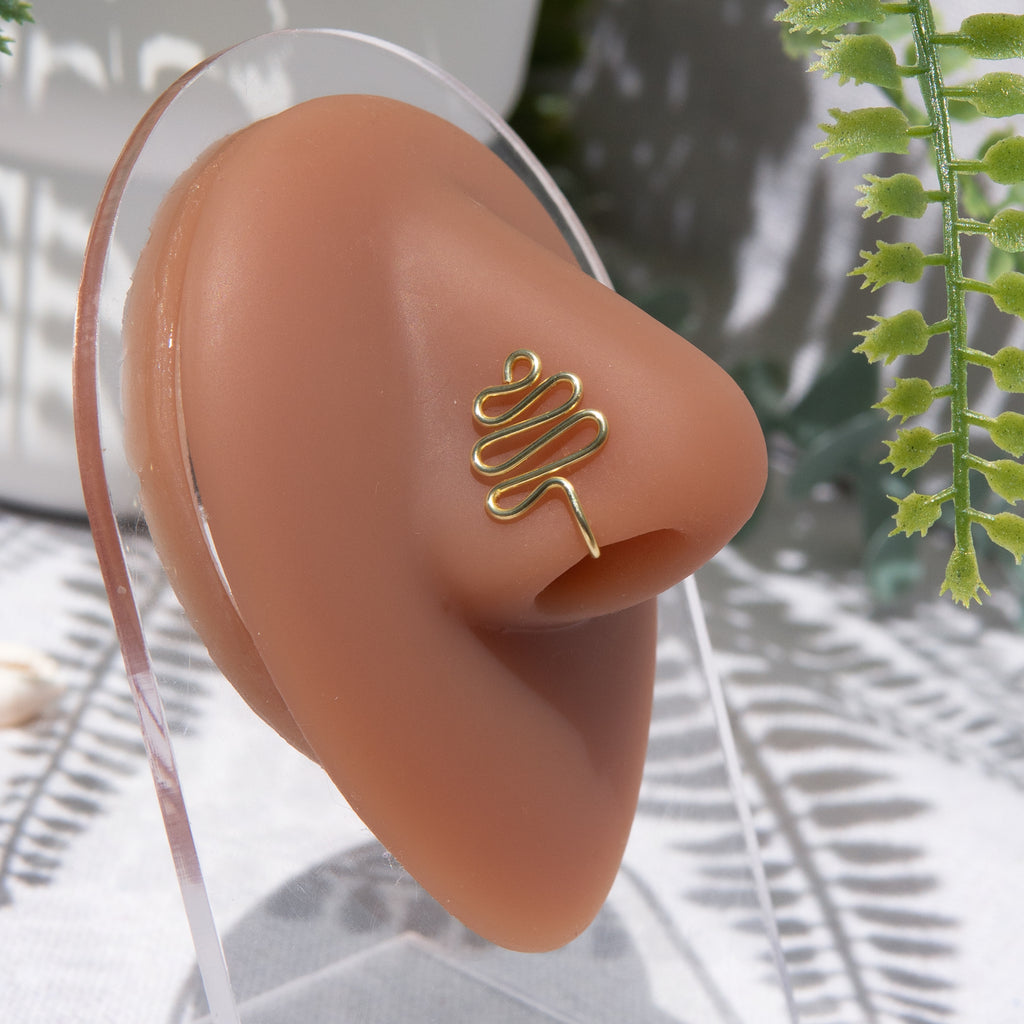 A gold-toned faux nose ring cuffs the model's nose. The wire design moulds a wavy pyramid shape.