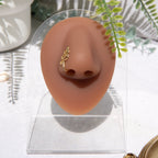 A gold-toned faux nose ring cuffs the model's nose. The wire design moulds a wavy pyramid shape.