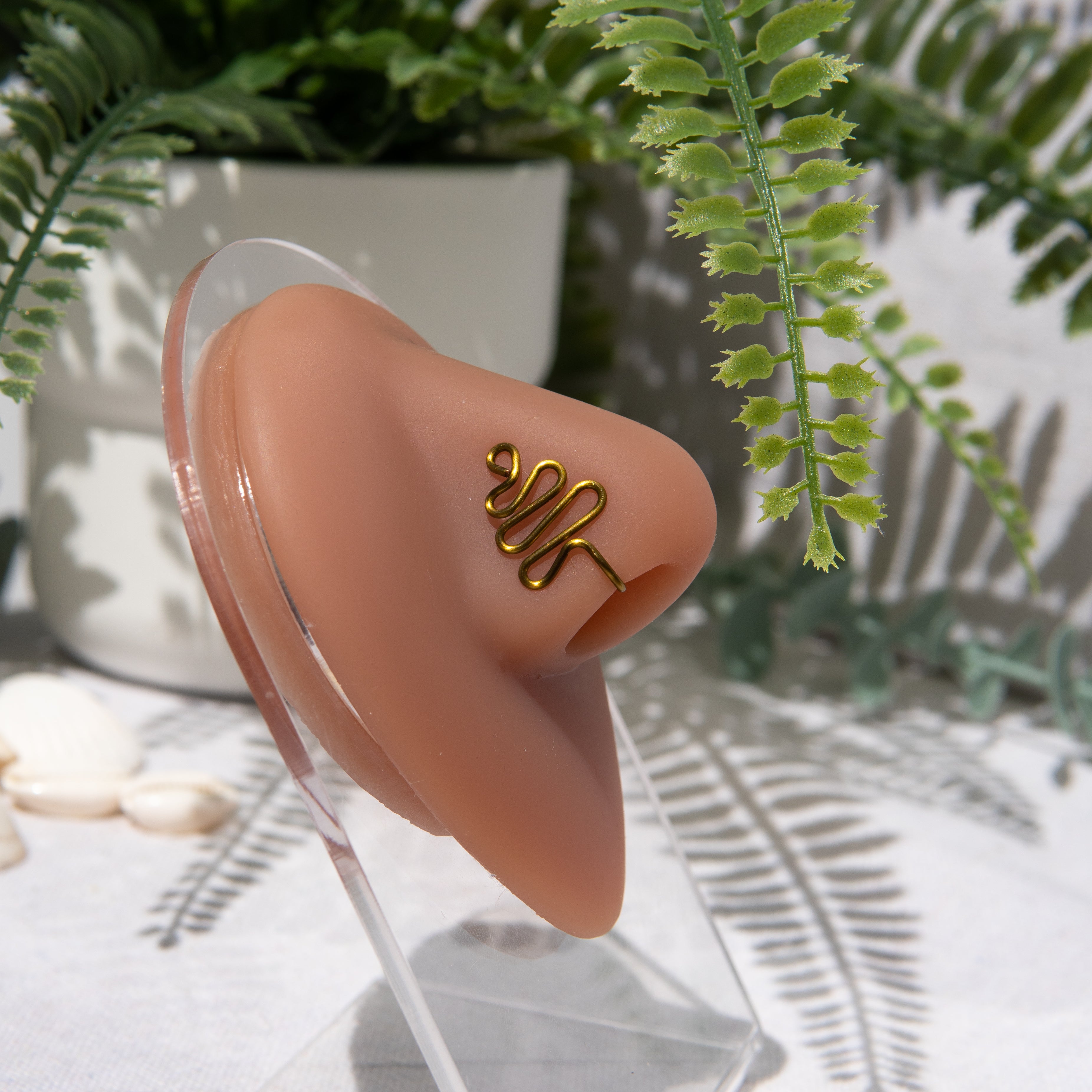 A gold-toned faux nose ring cuffs the model's nose. The wire design moulds a wavy pyramid shape.