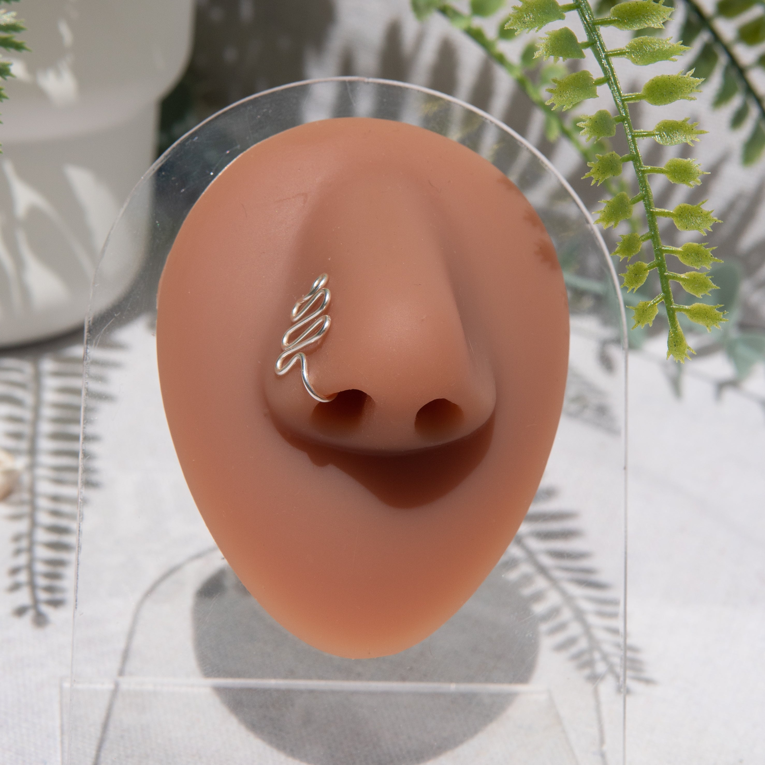 A silver faux nose ring cuffs the model's nose. The wire design forms a wavy pyramid shape.