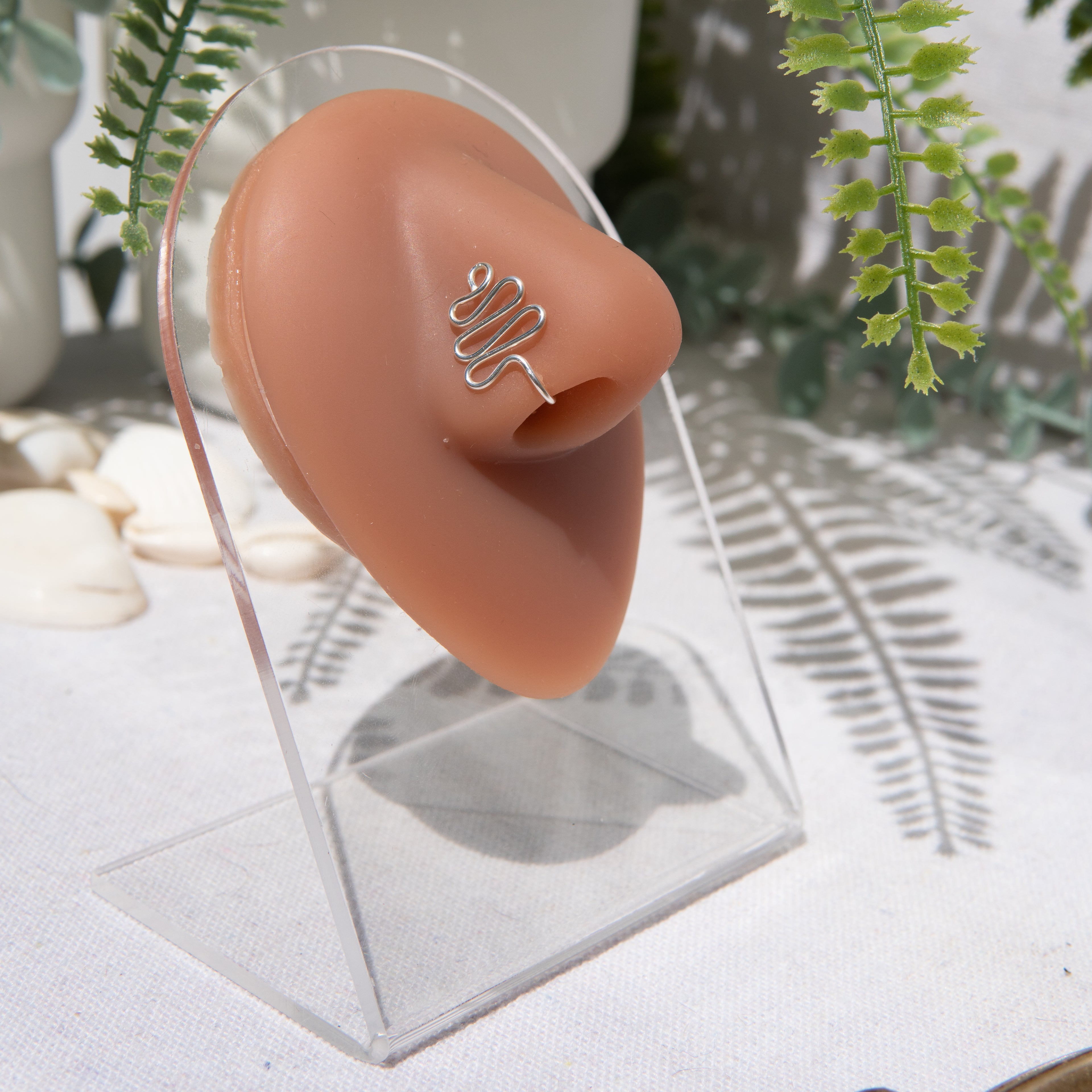 A silver-toned faux nose ring cuffs the model's nose. The wire design forms a wavy pyramid shape.