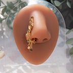 A gold-toned faux dangle nose ring cuffs the model's nostrils. Transparent mix of brown and green seed beads are wire-wrapped around the hoop's circumference, with three beaded gold curb chains dangling down.