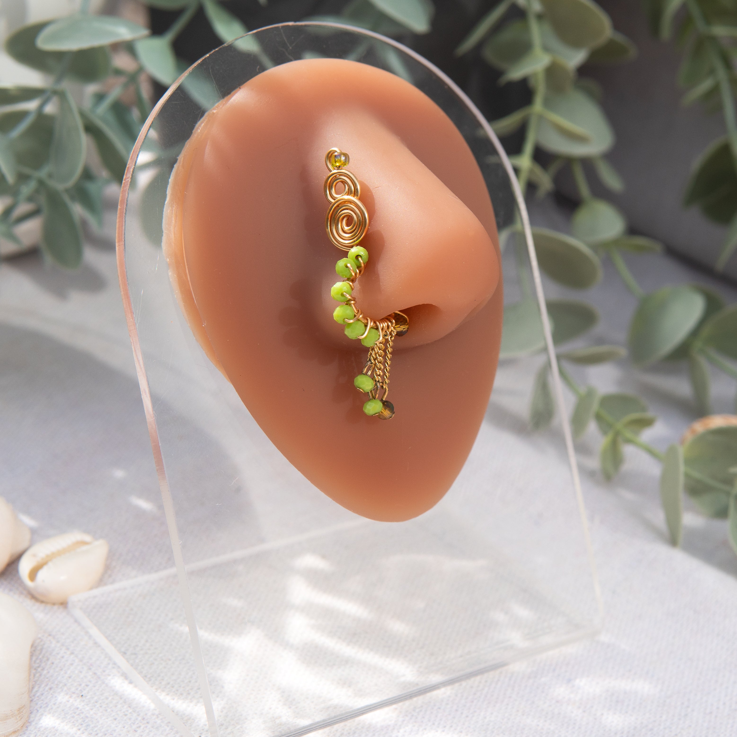 A light gold-toned faux dangle nose ring cuffs the model's nostrils. Green seed beads are wire-wrapped around the hoop's circumference, with three beaded gold chains dangling down.