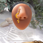 A gold-toned faux dangle nose ring cuffs the model's nostrils. Yellow seed beads are wire-wrapped around the hoop's circumference, with three beaded gold curb chains dangling down.