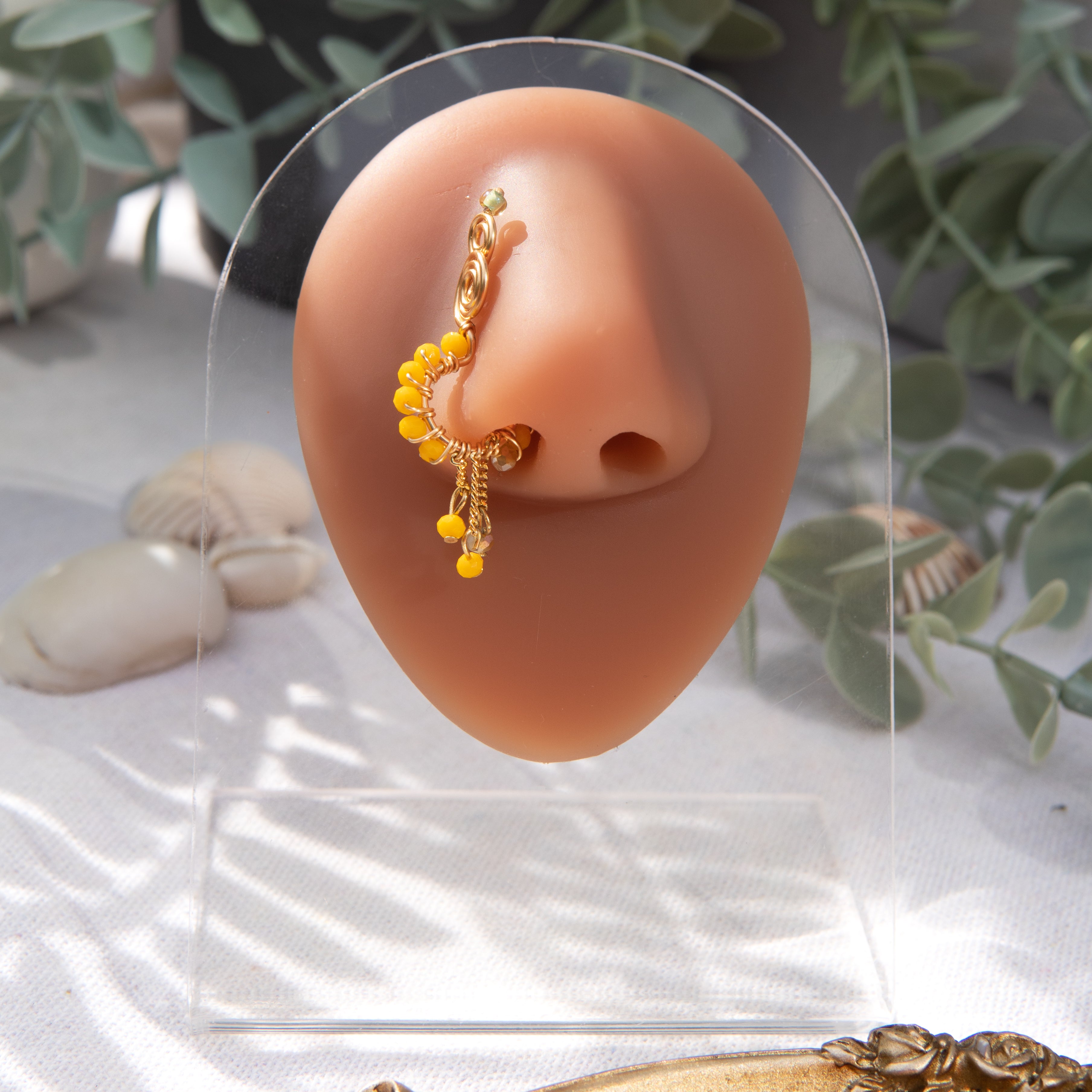 A gold-toned faux dangle nose ring cuffs the model's nostrils. Yellow seed beads are wire-wrapped around the hoop's circumference, with three beaded gold curb chains dangling down.