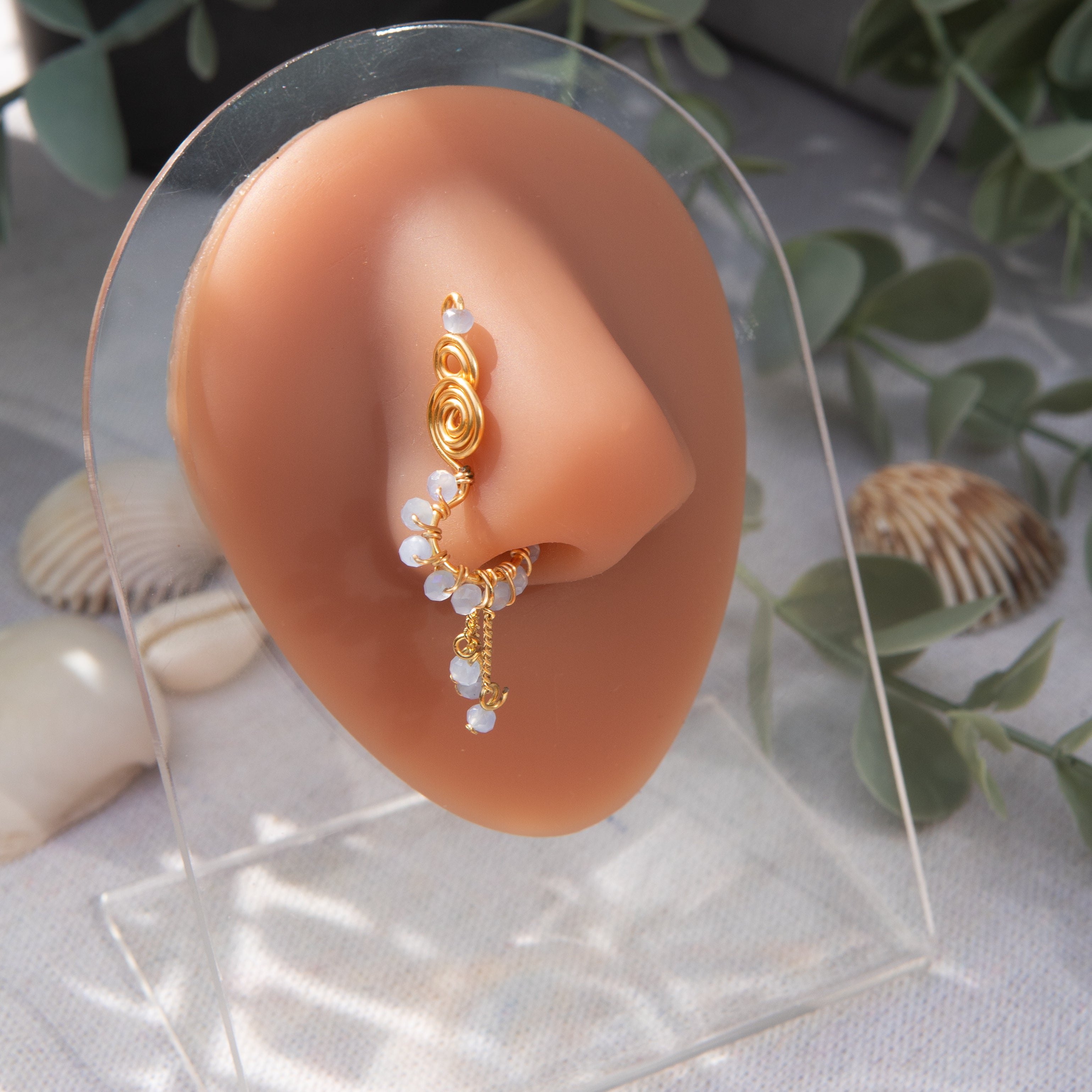 A gold-toned faux dangle nose ring cuffs the model's nostrils. Light blue seed beads are wire-wrapped around the hoop's circumference, with three beaded gold curb chains dangling down.