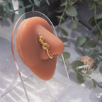 A light gold-toned, tightly spiralled nose cuff rests on the model's nose. Two seed beads (green and lilac) are interwoven into the design as the 3-tier circular spiral gradually decreases in size.