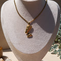 A gold-toned pendant necklace displayed on a textured off-white jewellery bust. The pendant is an Egyptian Queen Nefertiti