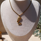 A gold-toned pendant necklace displayed on a textured off-white jewellery bust. The pendant is an Egyptian Queen Nefertiti