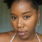 A gold-toned faux dangle nose ring cuffs the model's nostrils. A mix of brown and green transparent seed beads are wire-wrapped around the hoop's circumference, with three beaded gold curb chains dangling down.