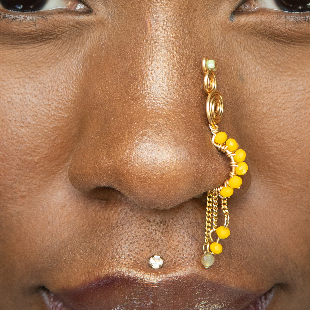 A gold-toned faux dangle nose ring cuffs the model's nostrils. Yellow transparent seed beads are wire-wrapped around the hoop's circumference, with three beaded gold curb chains dangling down.