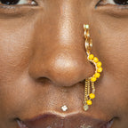 A gold-toned faux dangle nose ring cuffs the model's nostrils. Yellow transparent seed beads are wire-wrapped around the hoop's circumference, with three beaded gold curb chains dangling down.